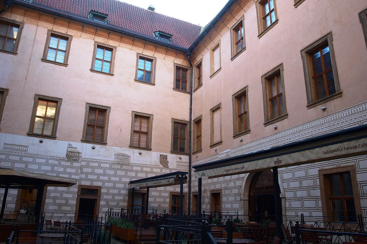 The inner courtyard of the Lobkowicz Palace with a sgraffito-decorated lower wall, pale upper storeys and café tables below